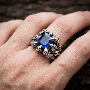 Gothic silver claw ring featuring a large rectangular blue sapphire gemstone gripped by dragon talons, worn on a man's finger