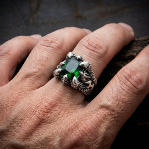 Gothic silver ring with large emerald green gemstone held by claw prongs and dragon scale detailing worn on a man's finger ag