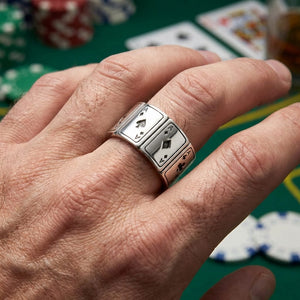 Close-up of a man's hand wearing a sterling silver Four Aces ring featuring engraved playing cards, set against a green poker