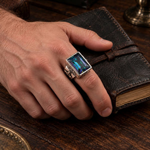 Sterling silver mystic quartz heraldic ring worn on a natural hand resting on a leather journal