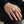 Sterling silver skull ring worn on a relaxed hand resting on a dark denim-covered knee.