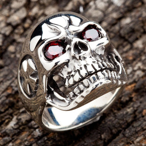 Dödskallering i högkvalitativt sterlingsilver med röda ögon presenterad mot trästruktur som visar detaljerat hantverk av bikersmycken