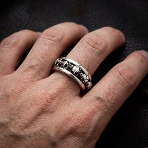 Sterling silver gothic skull ring with multiple skull designs worn on a man's finger against a dark textured background, show