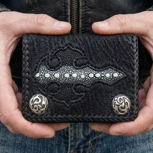 Black braided trifold held in both hands against a leather jacket and jeans, showing the stingray cross and two silver flame snaps.