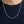 De gepolijste zilveren bolletjesketting valt over een marineblauw geribbeld shirt, waarbij de individuele kralen duidelijk zichtbaar zijn.