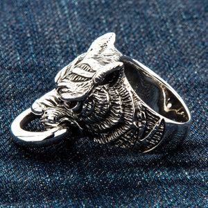 Vinklad närbild på denim: det morrande tigerhuvudet i sterlingsilver håller en slät ring mellan tänderna