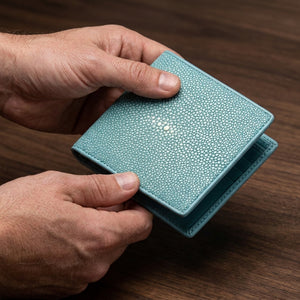 Turquoise stingray leather bifold wallet held slightly open in natural hands above a walnut counter