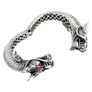 Vista obliqua del bracciale cuff a cerniera aperto con draghi che mostra le teste scolpite e l'interno.