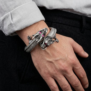 Bracciale cuff in argento a doppio drago con occhi di rubino indossato su un polso accanto a una manica grigia arrotolata.