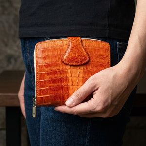 Two-Tone Orange Crocodile Leather Women's Wallet, held closed at hip level with the decorated front visible