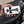 White cowhide biker wallet with black stingray cross held beside a black motorcycle seat