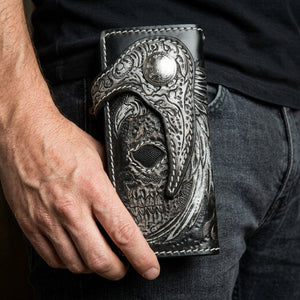 Billetera biker de raya con calavera alada y cierre en forma de gancho sostenida erguida a la altura de la cadera.