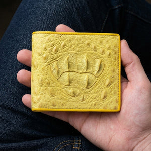Billetera bifold de cocodrilo hornback amarillo sostenida en manos de adulto